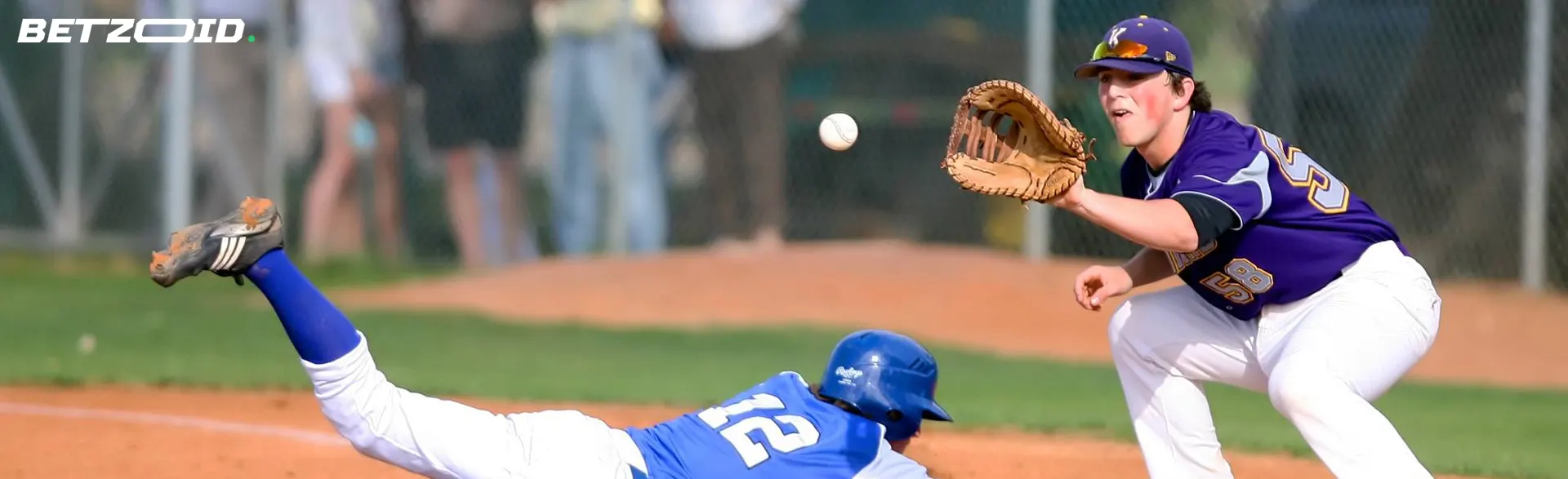 Un jugador de béisbol intenta atrapar una pelota en la base; otro jugador hace una entrada.