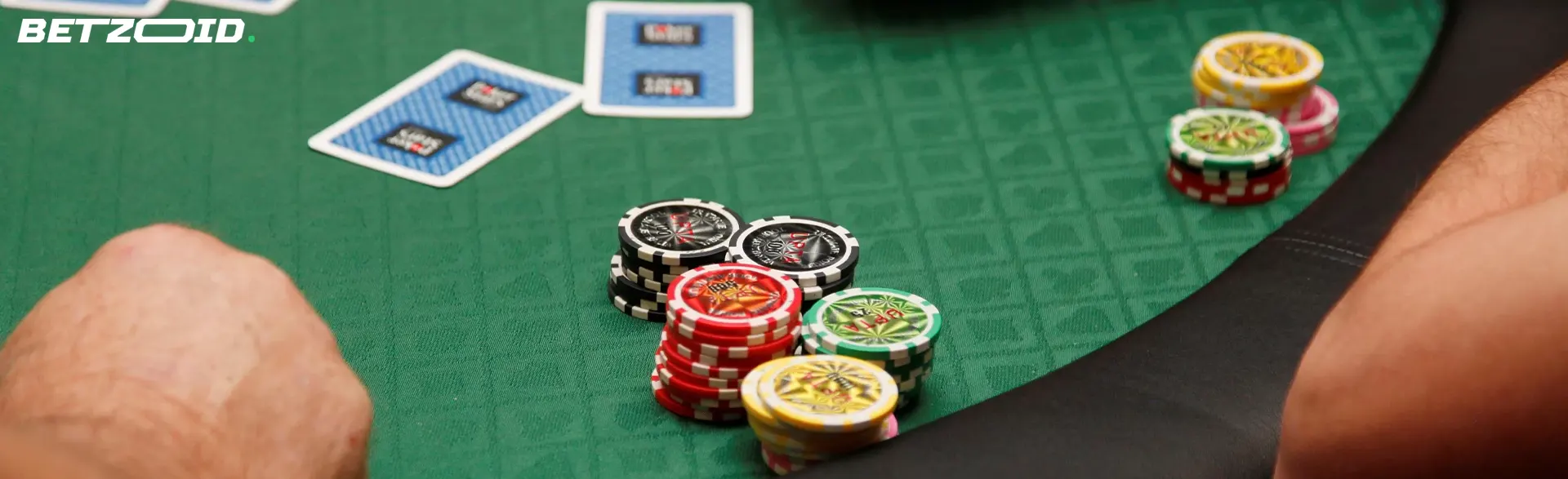 Mano che tiene due assi (cuori e picche) con fiches da poker sul tavolo rosso.