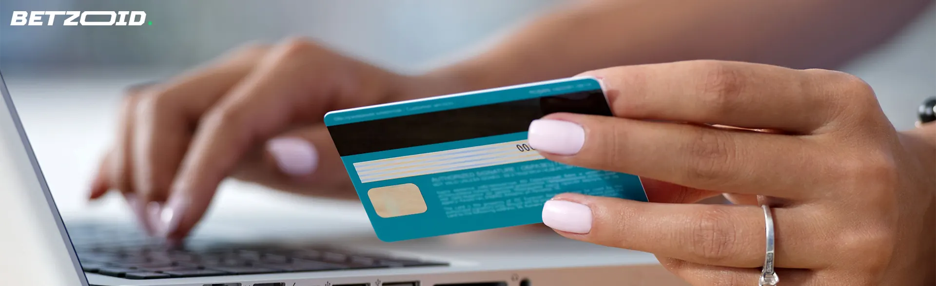Cartão de crédito na mão de um homem em frente a um laptop.